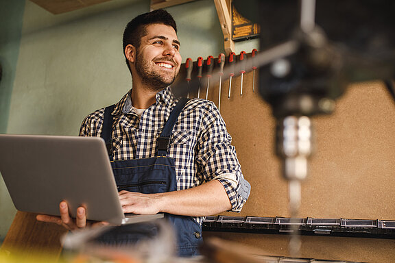 Ein Handwerker arbeitet in einer Werkstatt mit einem Laptop.